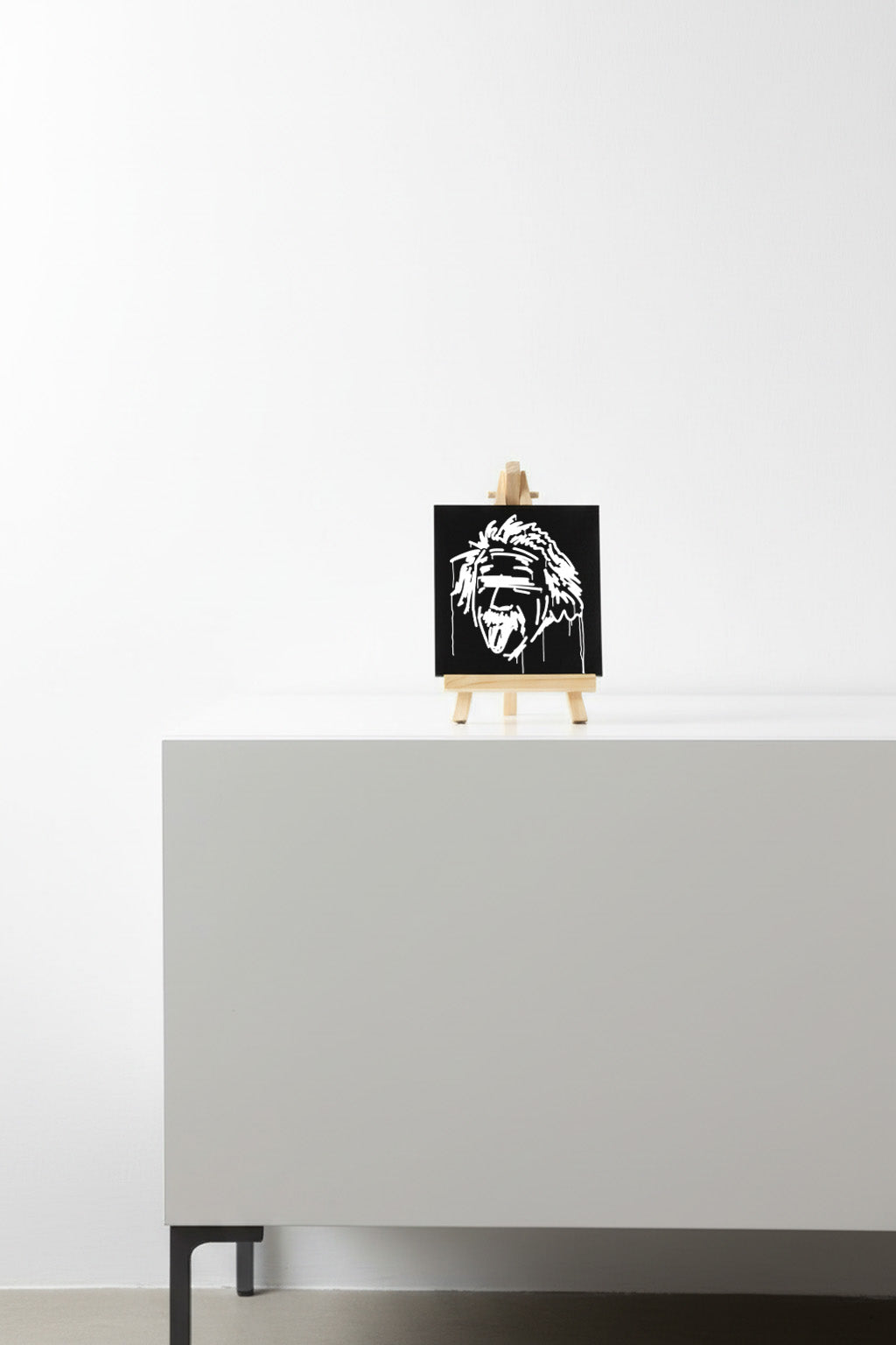 Designspiegel Mini mit Einstein-Motiv auf kleiner Holzstaffelei, dekorativ auf einem modernen Sideboard platziert.