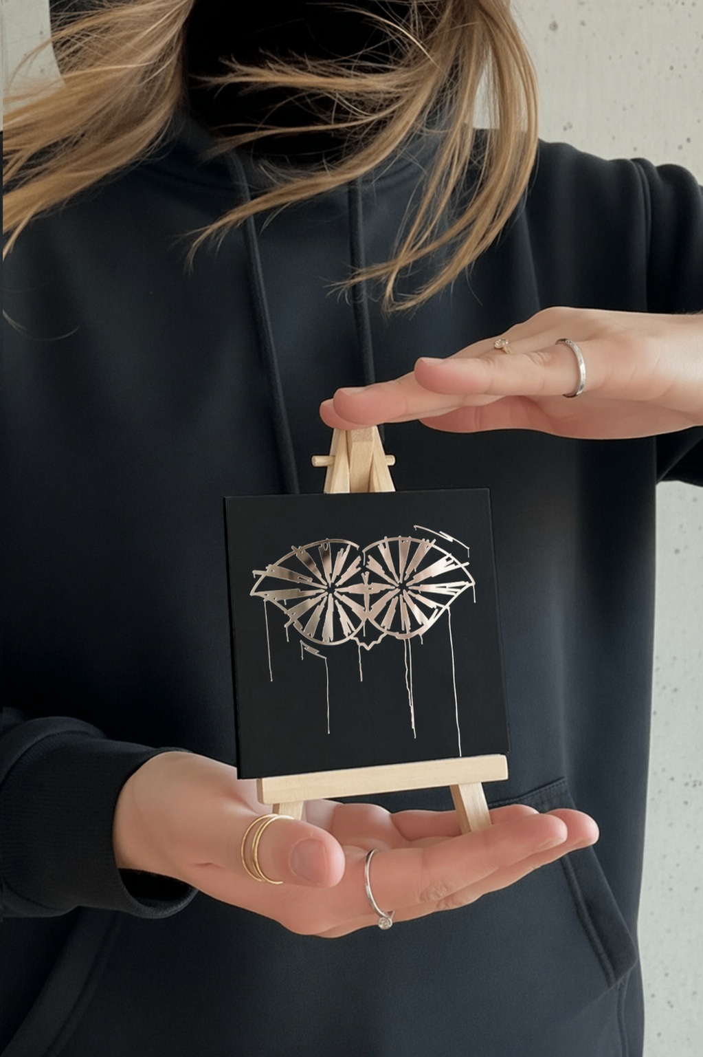 Person hält einen 10 × 10 cm großen Designspiegel Mini mit spiegelndem Motiv Schneider von Ulm
