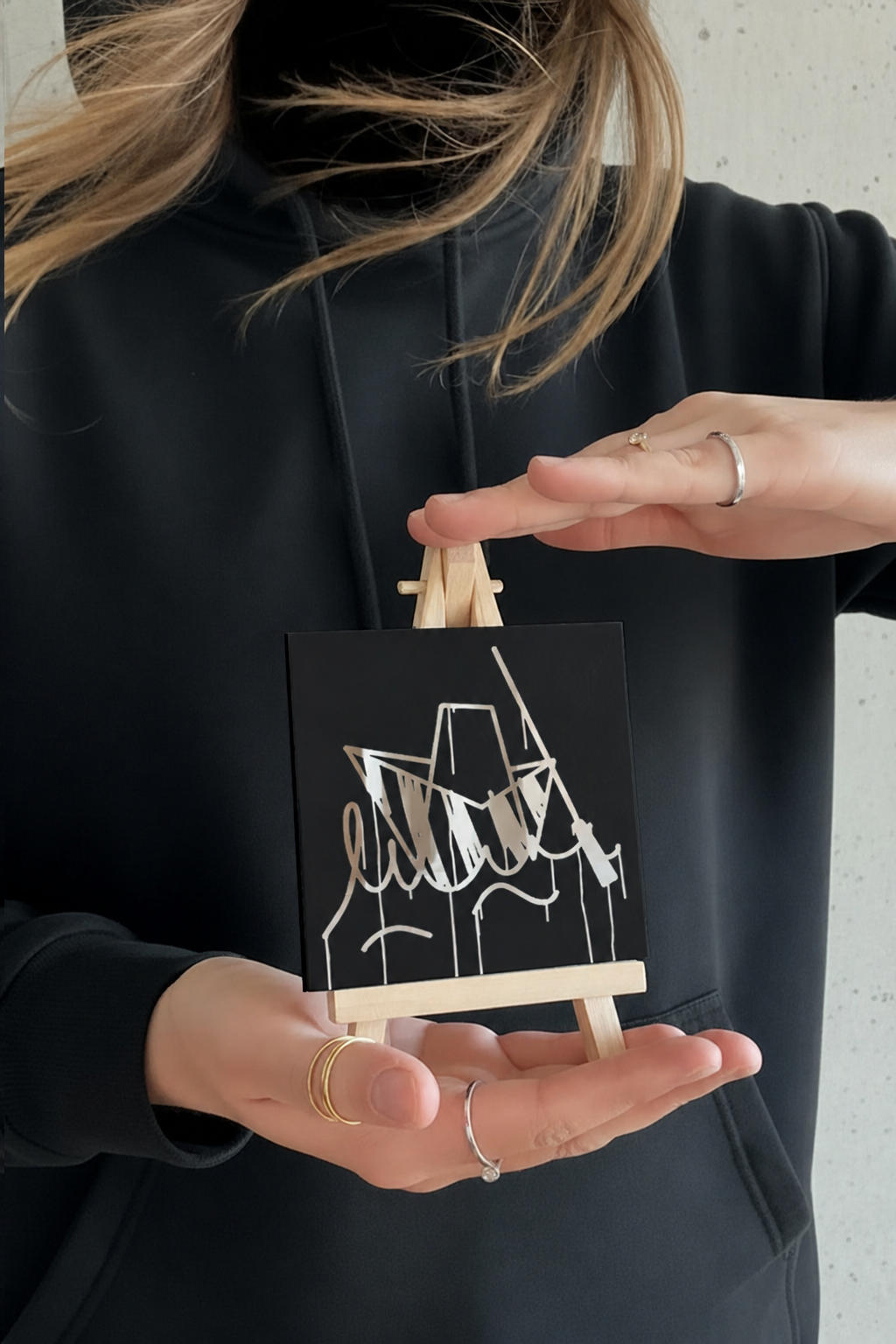 Person hält einen 10 × 10 cm großen Designspiegel Mini mit spiegelndem Motiv Ulmer Schachtel
