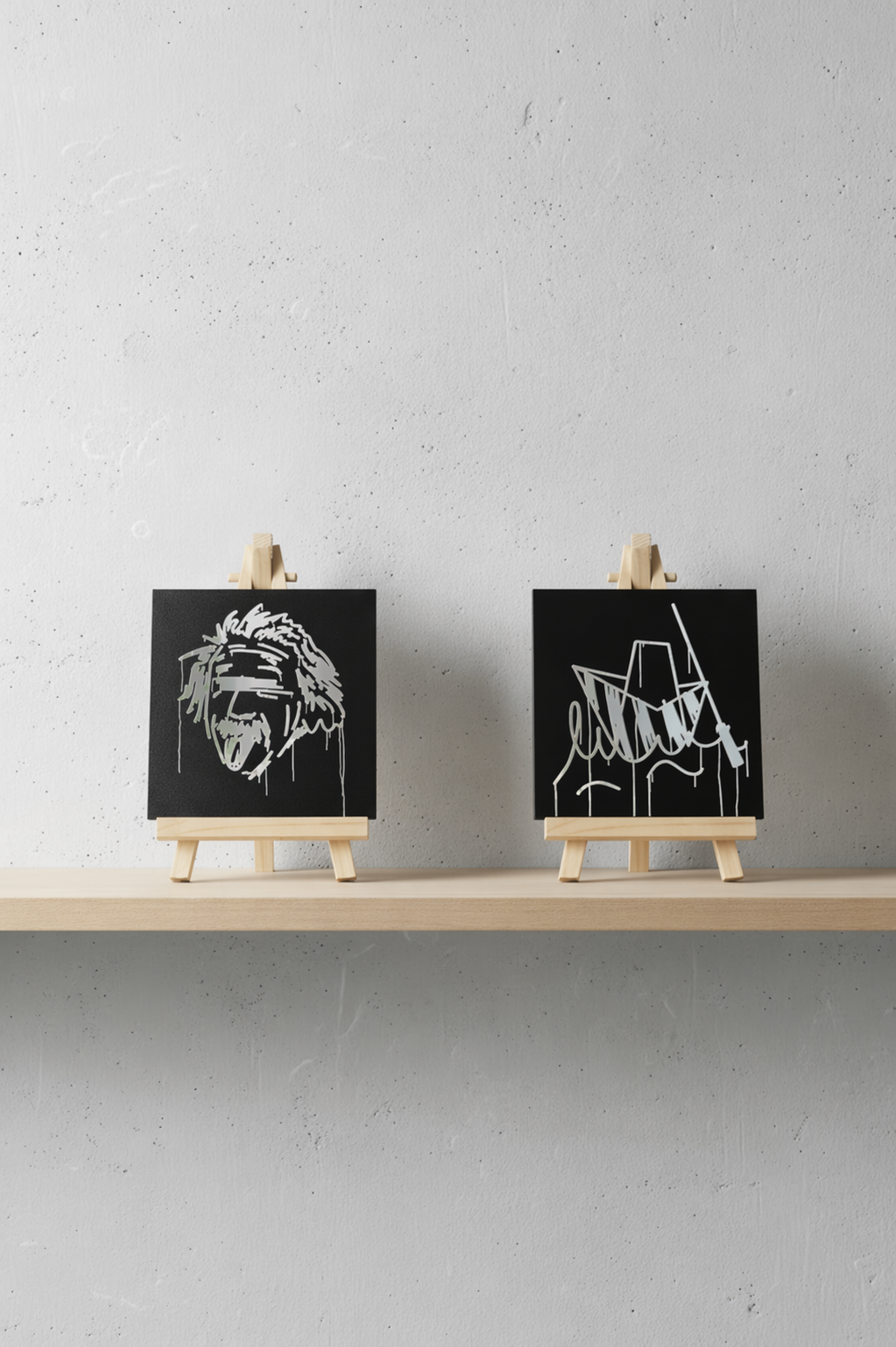 Zwei schwarze Designspiegel Mini mit spiegelnden Motiven Albert Einstein und Ulmer Schachtel auf einem Holzregal

