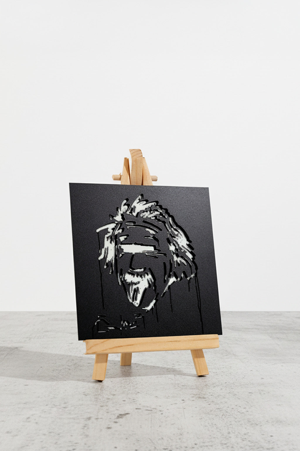 Designspiegel Mini mit Einstein-Motiv auf kleiner Holzstaffelei, leicht seitlich fotografiert auf hellem Untergrund.