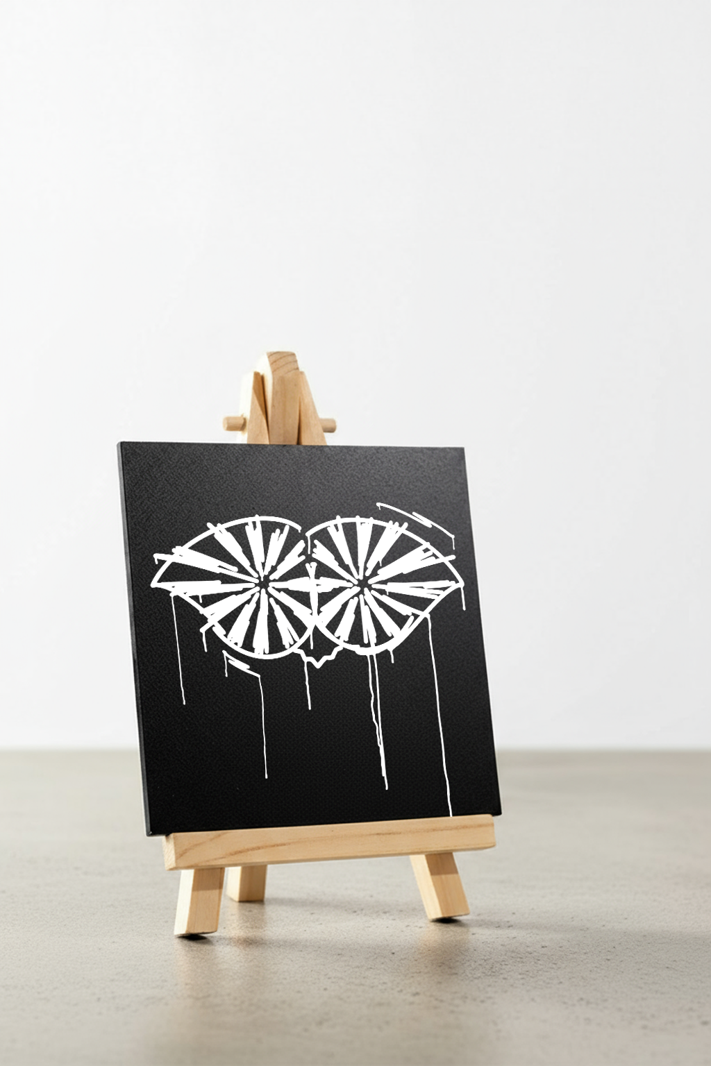 Designspiegel Mini Schneider von Ulm in schräger Ansicht auf Holzstaffelei, schwarzer Spiegel mit weißem Urban-Art-Design – stilvolle moderne Deko