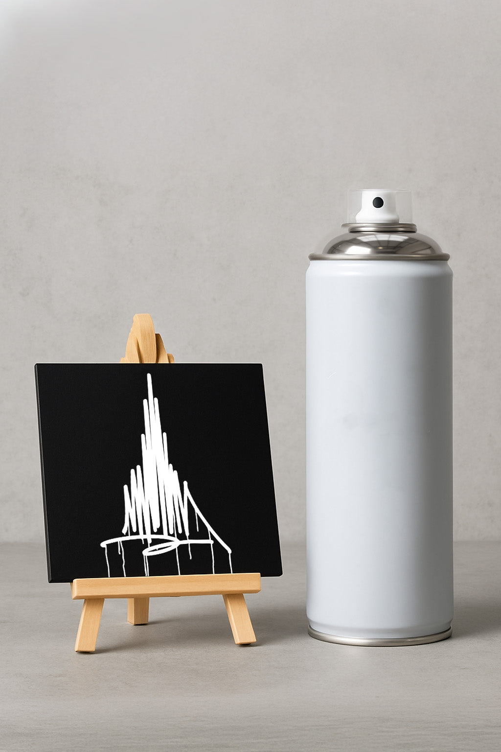 Schwarzer Designspiegel Mini mit weißem Münster-Urban-Art-Motiv auf Holzstaffelei neben einer 400-ml Sprühdose als Größenvergleich.