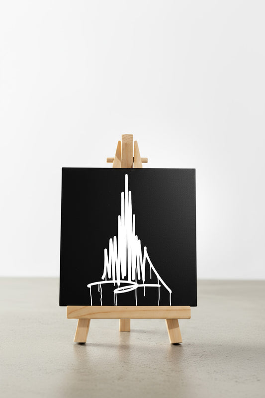 Schwarzer Designspiegel Mini mit weißem Münster-Urban-Art-Motiv, frontal auf einer kleinen Holzstaffelei auf hellem Boden präsentiert.