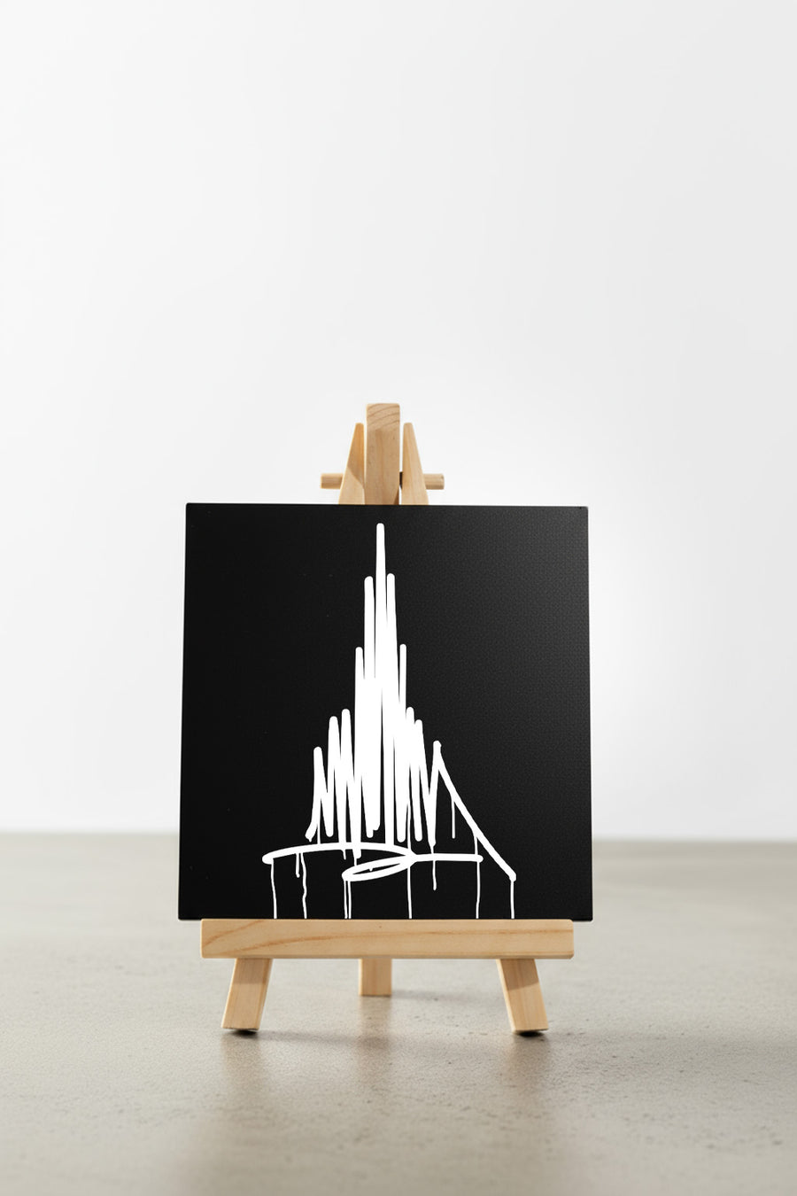 Schwarzer Designspiegel Mini mit weißem Münster-Urban-Art-Motiv, frontal auf einer kleinen Holzstaffelei auf hellem Boden präsentiert.