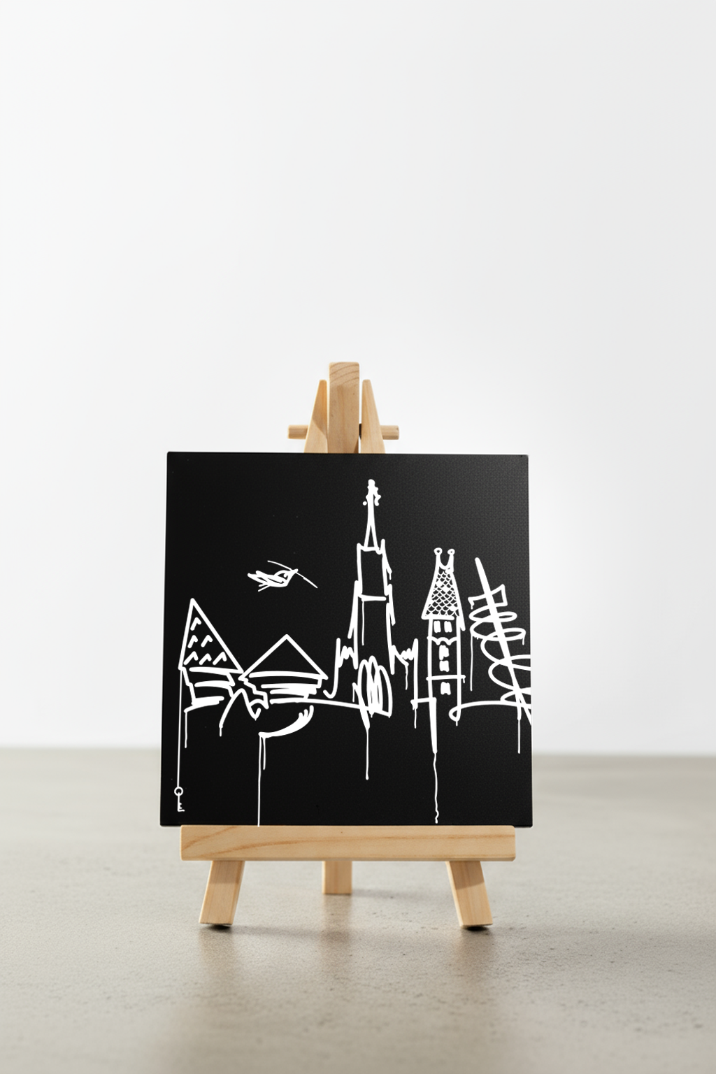 Designspiegel Mini mit Ulm Skyline, minimalistische weiße Linien auf schwarzem Hintergrund, frontal auf kleiner Holzstaffelei präsentiert.