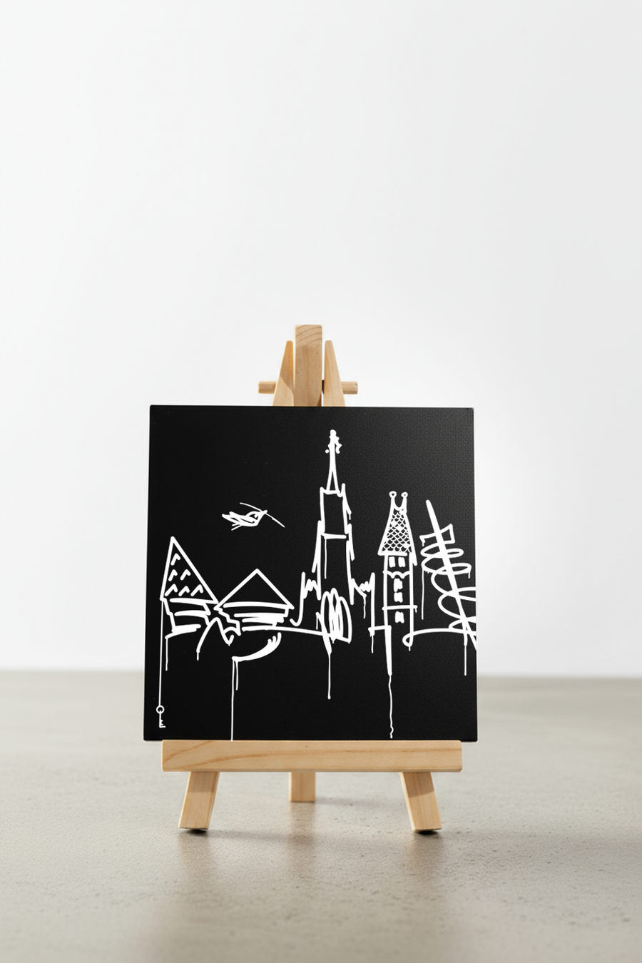 Designspiegel Mini mit Ulm Skyline, minimalistische weiße Linien auf schwarzem Hintergrund, frontal auf kleiner Holzstaffelei präsentiert.