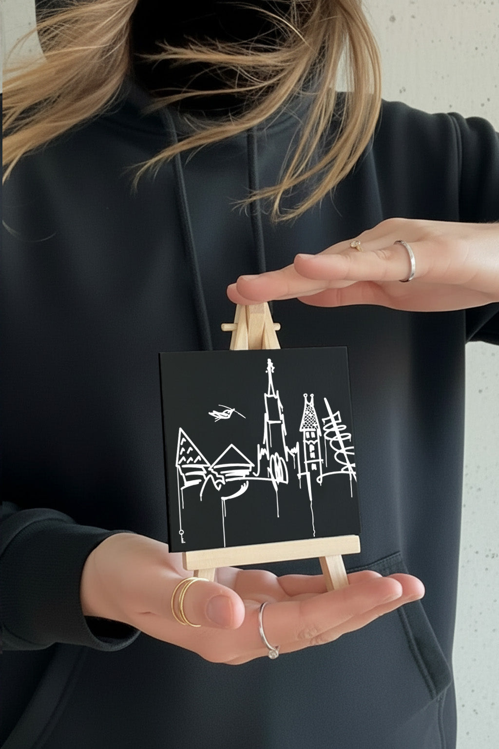 Kleiner Designspiegel Mini mit Ulm Skyline, von einer Person im schwarzen Hoodie gehalten, urbanes minimalistisches Kunstmotiv.