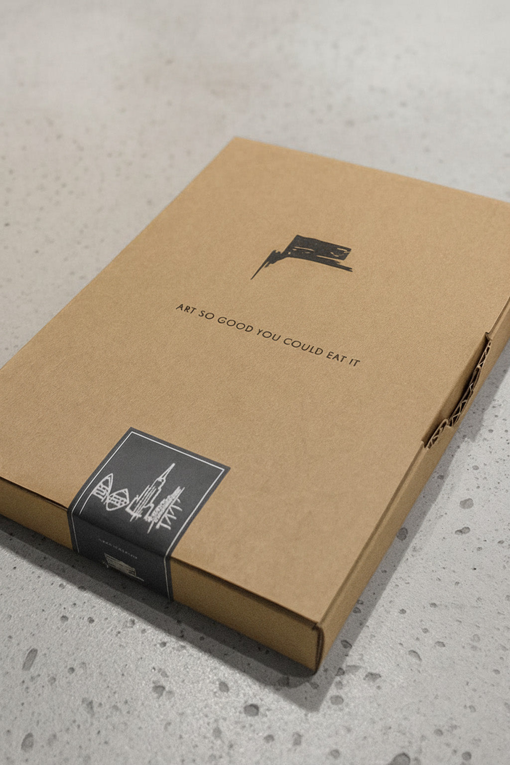 Hochwertige Versandverpackung des Designspiegel Mini aus kraftbraunem Karton mit Urban-Art Branding und schwarzem Motivband auf Betonoberfläche.