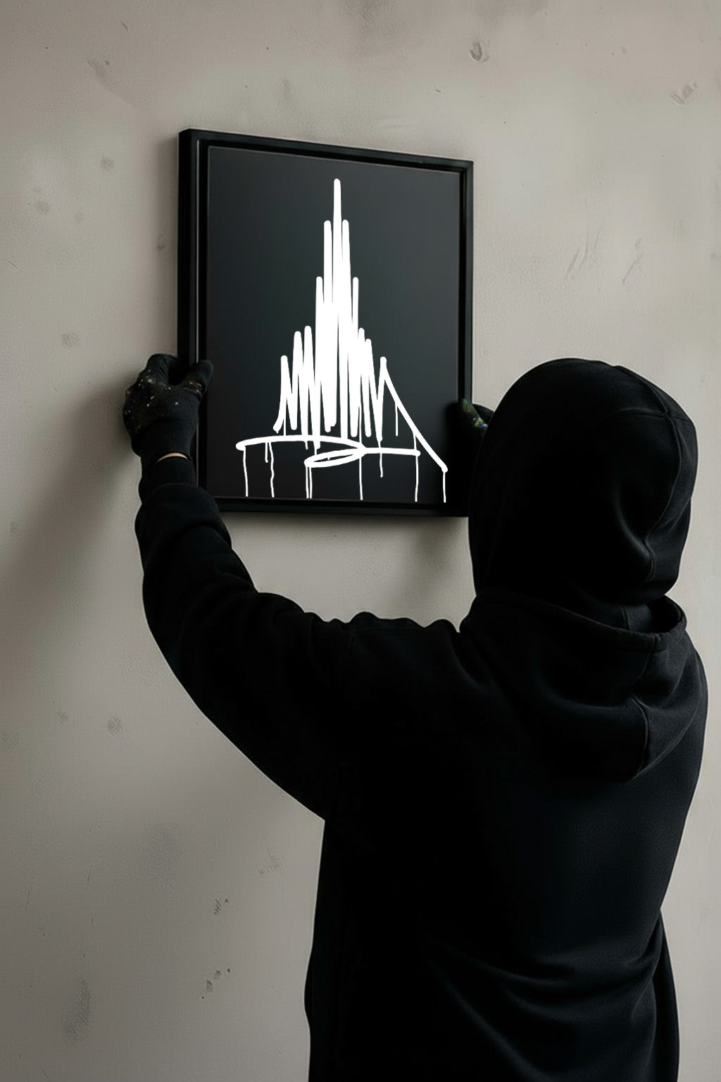 Person in schwarzem Hoodie hängt einen matt schwarzen Designspiegel im Format 40×50 cm mit spiegelndem Urban-Art-Motiv des Ulmer Münsters an eine Wand.