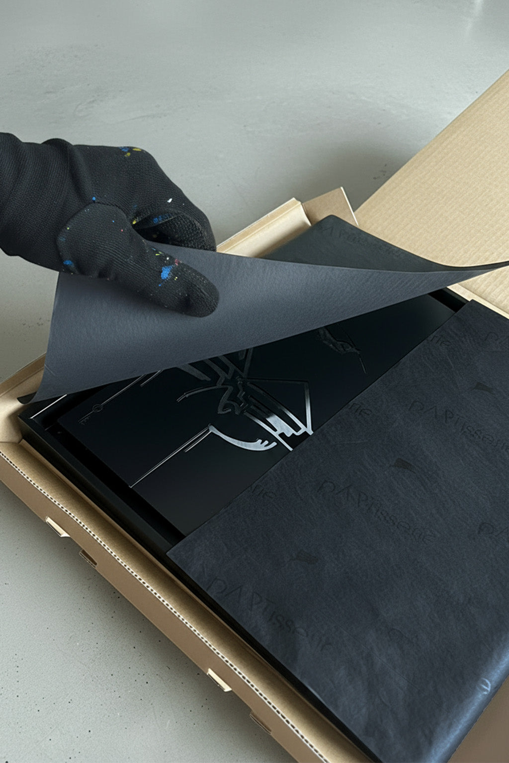 Auspacken eines hochwertigen Designspiegels in mattschwarzer Urban-Art-Optik; schwarze Schutzfolie wird von Hand entfernt, Premium-Verpackung mit pARTisserie-Seidenpapier