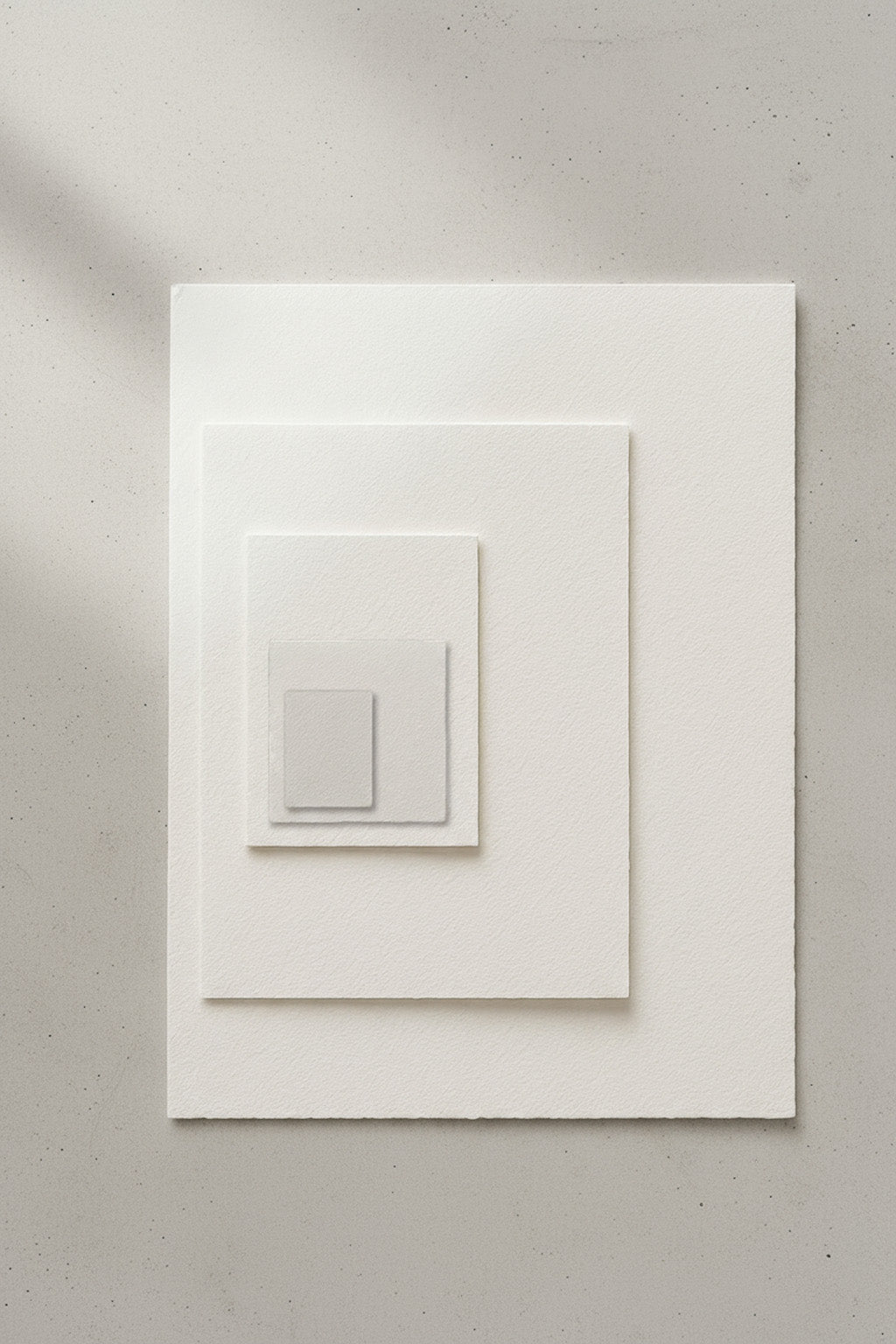 Mehrere übereinanderliegende Aquarellpapiere in verschiedenen Größen, als Größenvergleich auf hellem Betonuntergrund präsentiert.